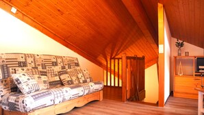 Ein gemütliches Schlafzimmer im Loft-Stil mit schrägem Dach, einem hölzernen Bett mit gemusterten Bettbezügen und einem kleinen Holztisch mit Fernseher.