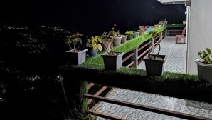 A balcony with potted plants, a green artificial grass barrier, and a view of the city at night. - LuxeHaven Homestay-a Peaceful Escape (Darjeeling)