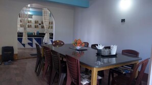 A dining area with a table, chairs, a vase with flowers, and a kitchen visible through a doorway. - LuxeHaven Homestay-a Peaceful Escape (Darjeeling)