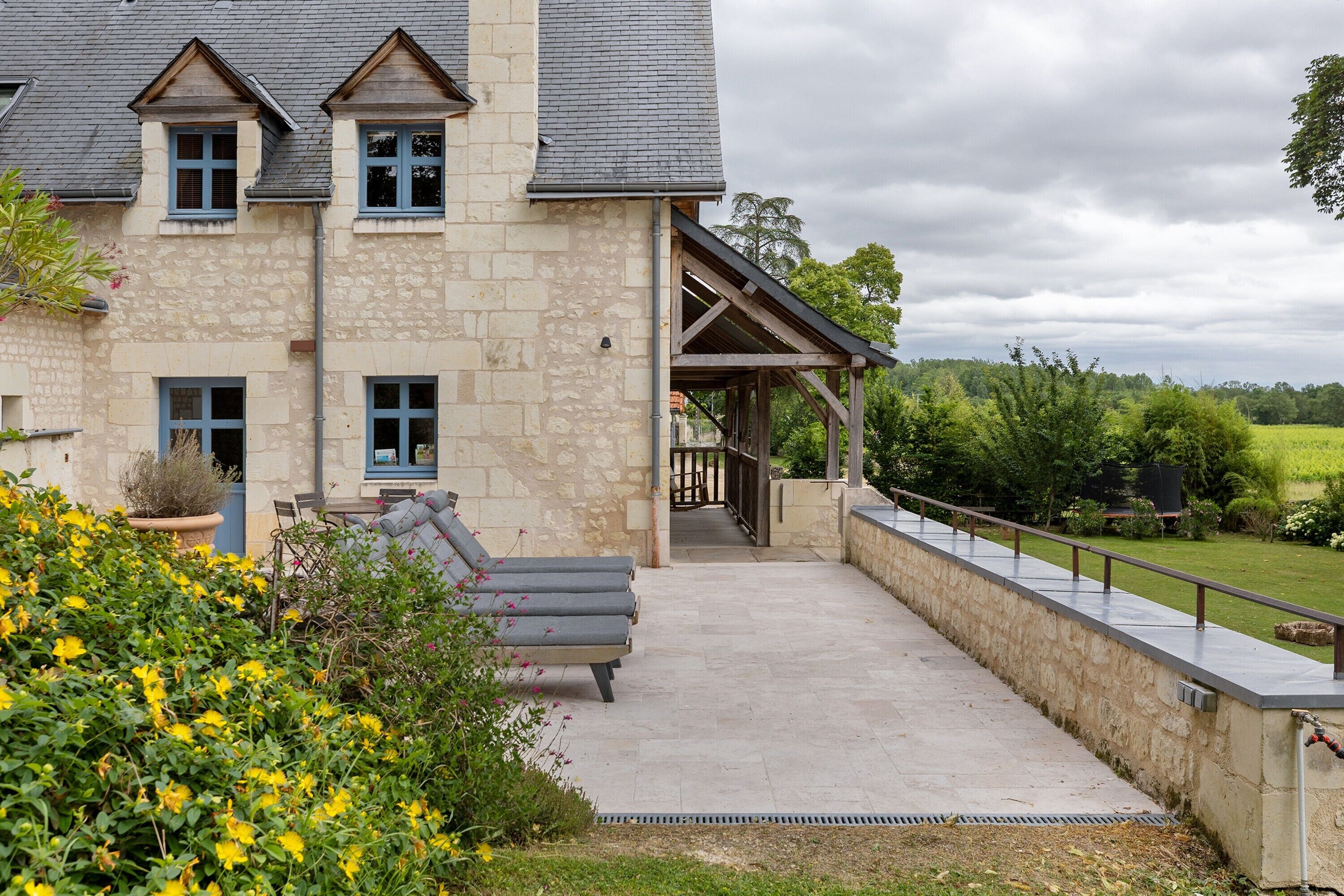 A stone building with a covered patio, a bench, and a view of a green landscape.
