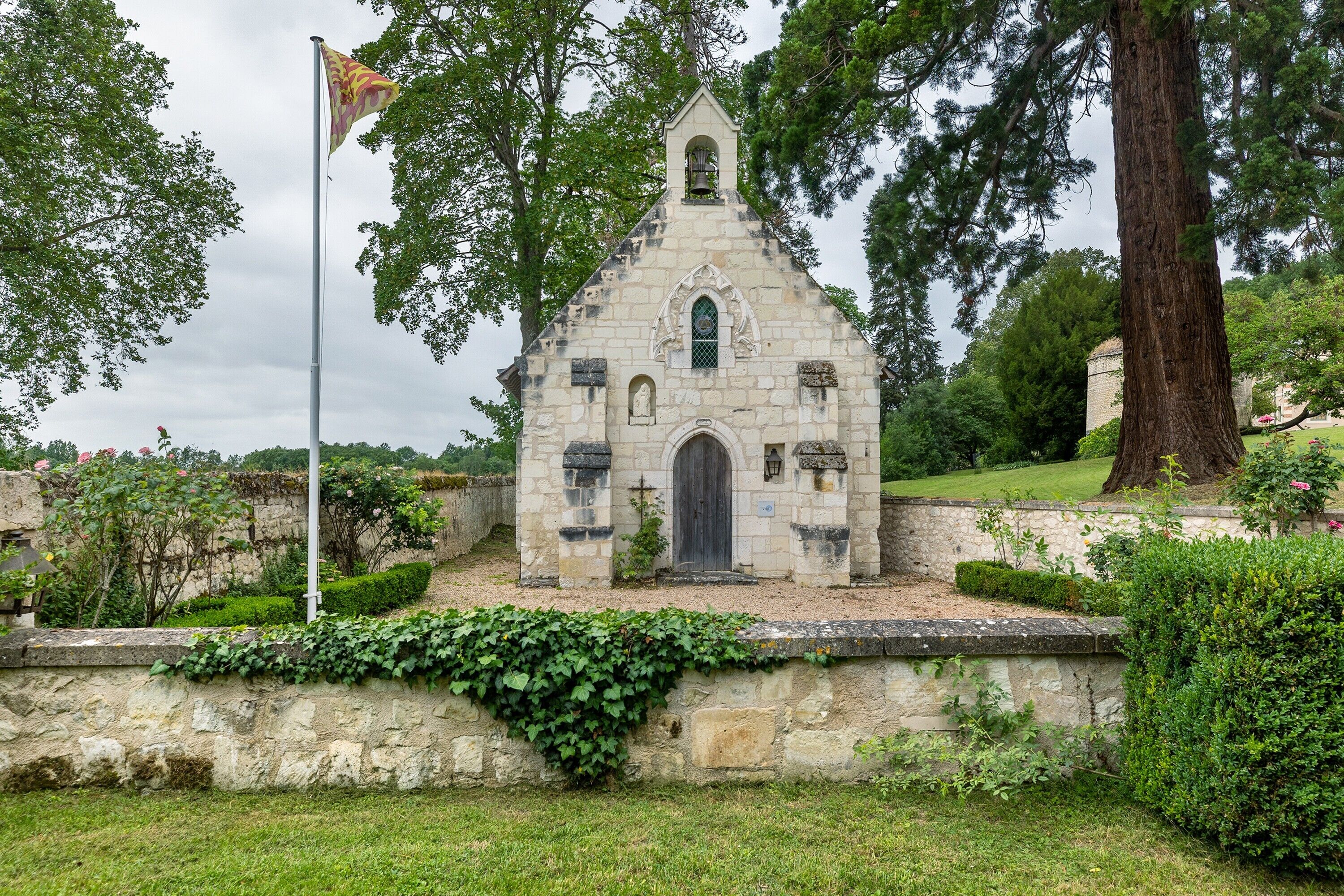 A stone church with a bell tower, surrounded by greenery and a flagpole.