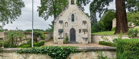 A stone church with a bell tower, surrounded by greenery and a flagpole.
