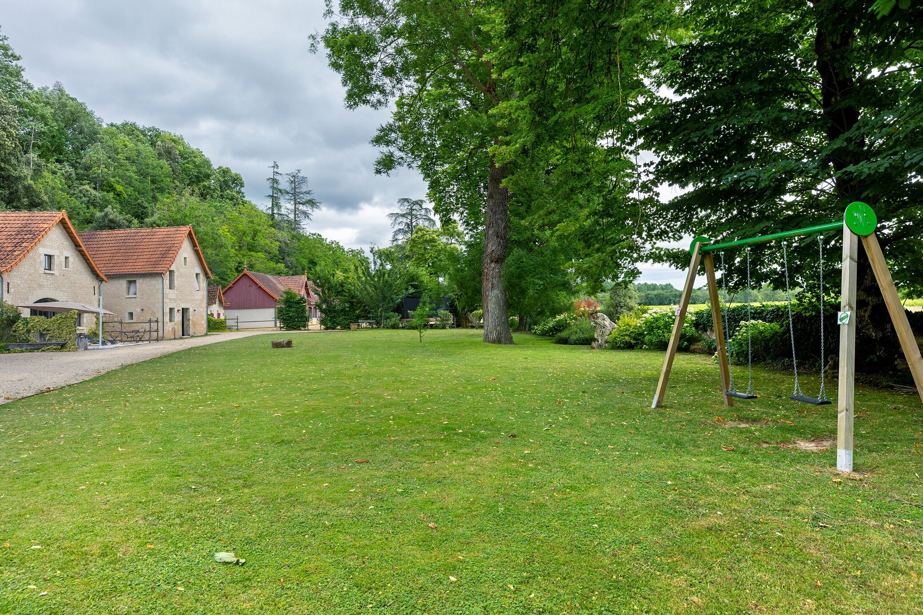 Une zone herbeuse avec une balançoire, un bâtiment avec un toit rouge et un grand arbre.