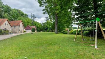 Une zone herbeuse avec une balançoire, un bâtiment avec un toit rouge et un grand arbre.