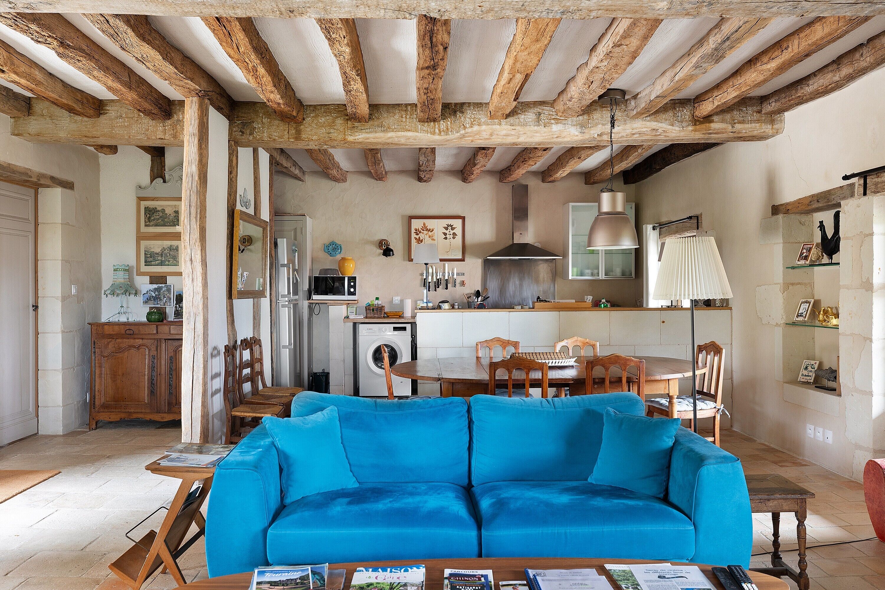 Un soggiorno con divano blu, tavolo da pranzo in legno e cucina sullo sfondo.