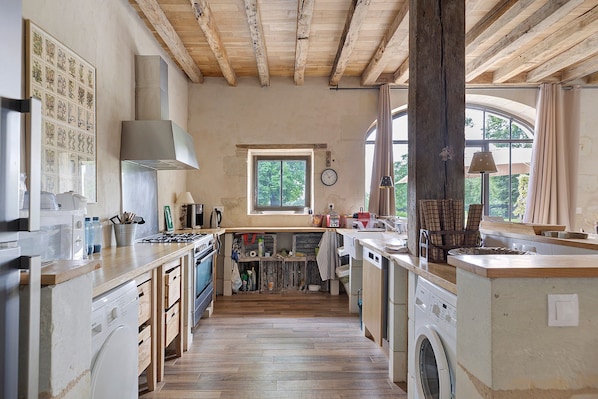Una cocina con vigas de madera, lavadora y ventana con cortinas.