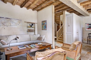 A living room with a sofa, coffee table, and wicker chairs. There is a staircase leading to another room. - La Motte Wilhelm de Sonnay – Relais du Château de Sonnay (Cravant-les-Côteaux)