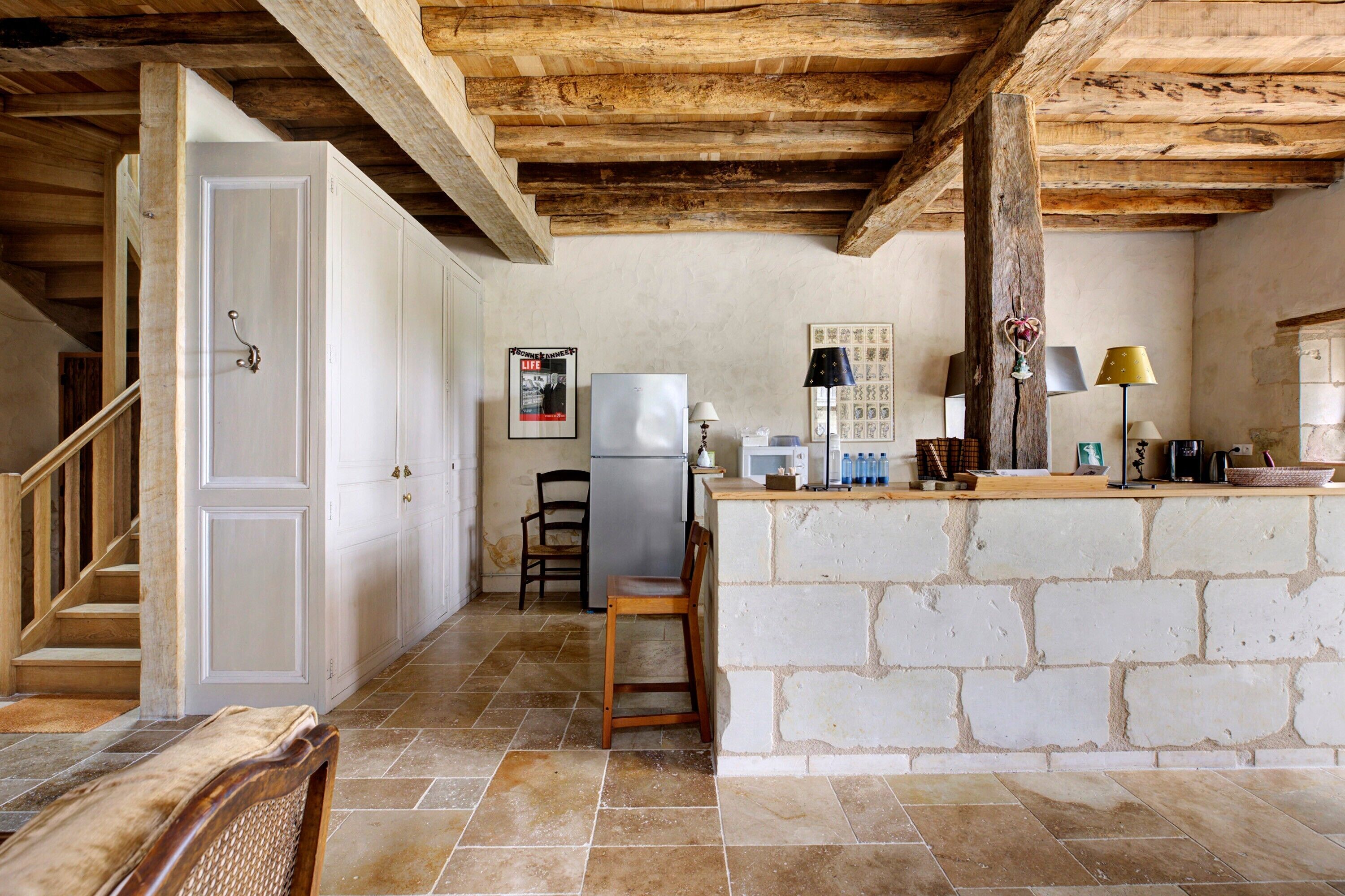 Une cuisine avec des murs en pierre, un plafond en bois, un réfrigérateur et un coin bar.
