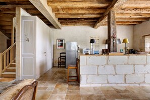 Una cocina con paredes de piedra, techo de madera, un refrigerador y una barra.