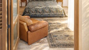 Een slaapkamer met een bed, een bankje, een vloerkleed, een schilderij en twee bedlampjes.
