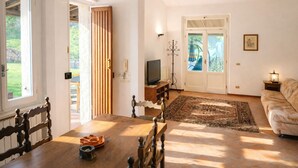 Een woonkamer met een houten eettafel, een bank, een televisie en een deur naar een balkon.