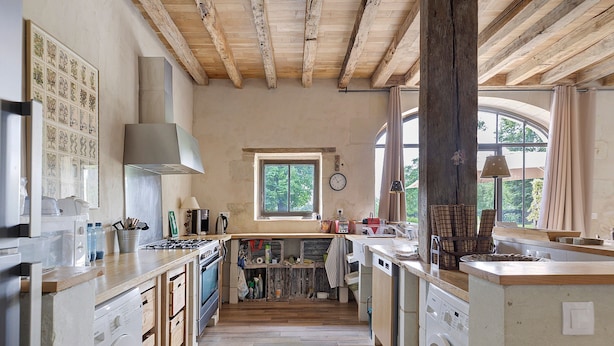 Una cocina con vigas de madera, lavadora y ventana con cortinas.