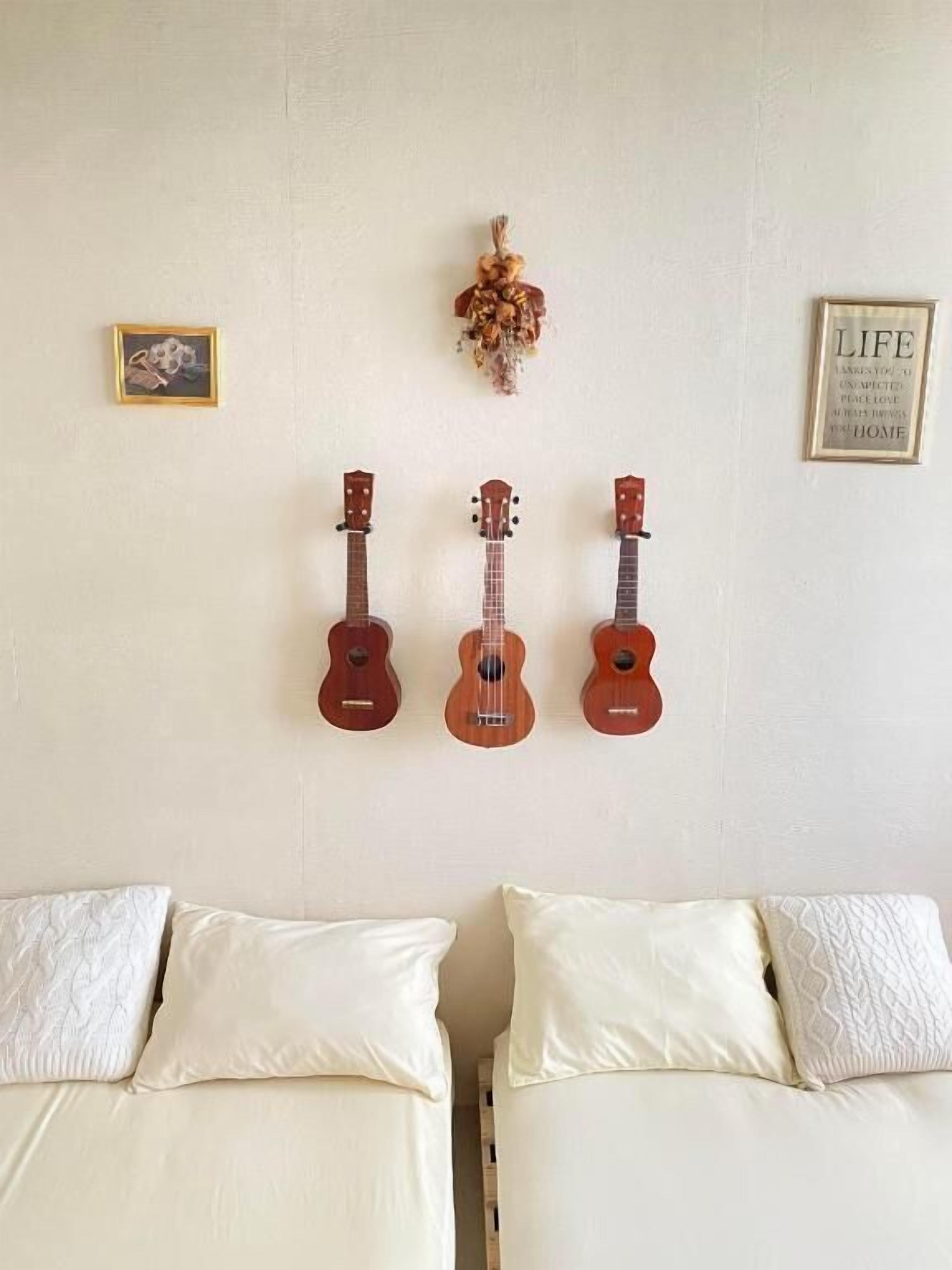 Quarto com três ukuleles fixados na parede, duas camas com roupa de cama branca e dois objetos emoldurados nas paredes.