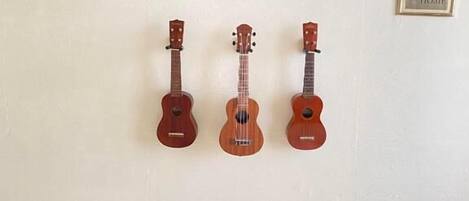 Quarto com três ukuleles fixados na parede, duas camas com roupa de cama branca e dois objetos emoldurados nas paredes.