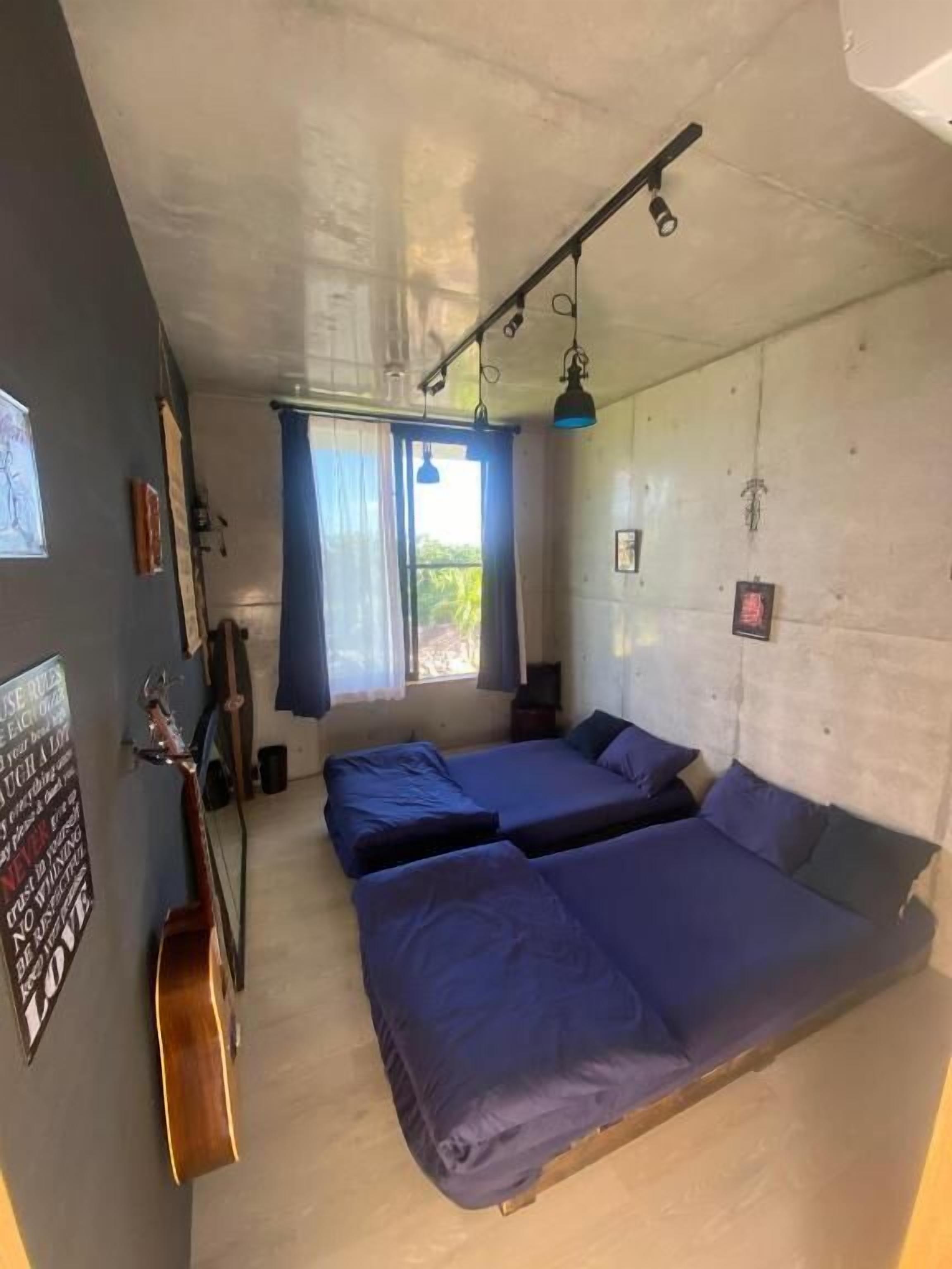 Een kamer met twee bedden, een gitaar, een raam met gordijnen en een poster aan de muur.