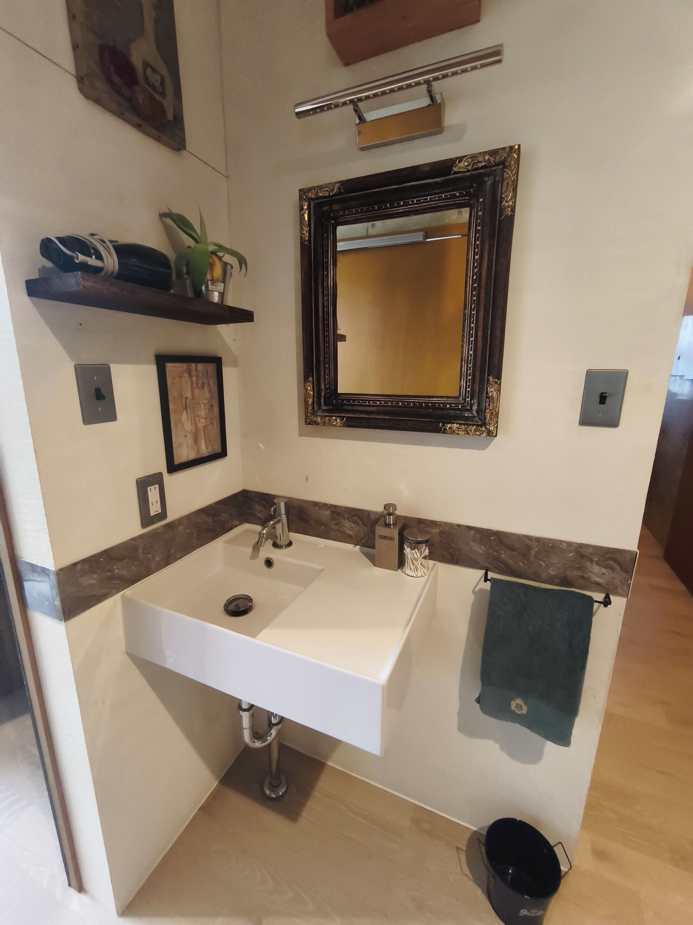 A bathroom with a white sink, a mirror, a towel rack, and a shelf with a plant.