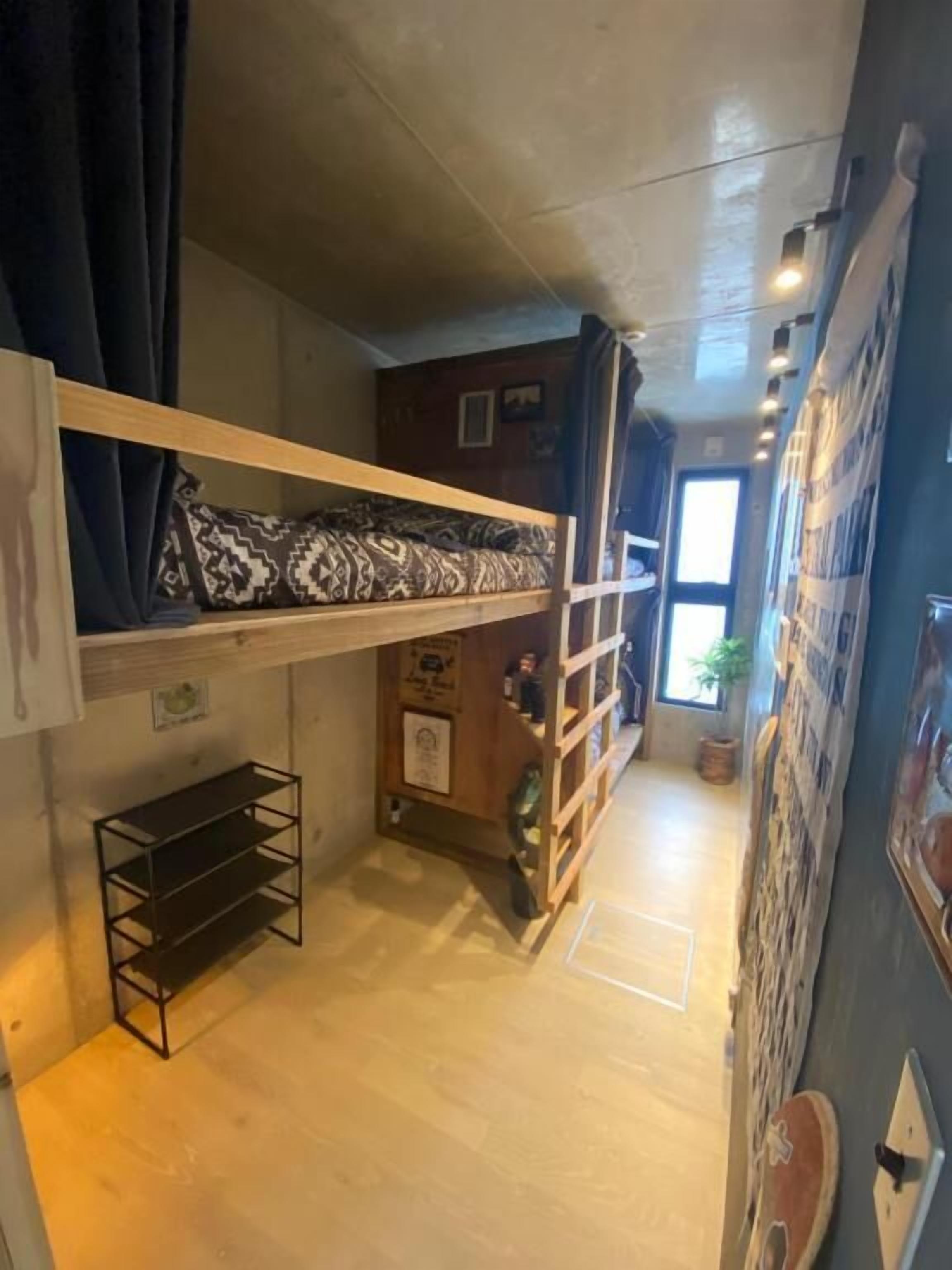 A compact room with a bunk bed, a small shelf, and a wall-mounted rack.