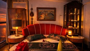 A bed with a red upholstered headboard, a bedside table with a lamp, a painting on the wall, and a cabinet with glass doors. - 康宿·夕观居｜日落海景双卧套房
KanStay Sunset View | 2BR Sunset Ocean View Suite (Manila)