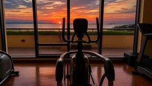 A room with a view of a sunset over water, a chair, and a treadmill. - 康宿·夕观居｜日落海景双卧套房
KanStay Sunset View | 2BR Sunset Ocean View Suite (Manila)