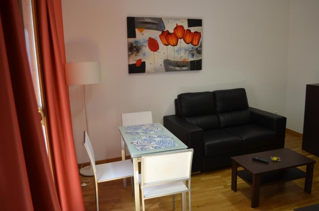 Un salon avec un canapé noir, une petite table, une chaise blanche et un tableau accroché au mur.