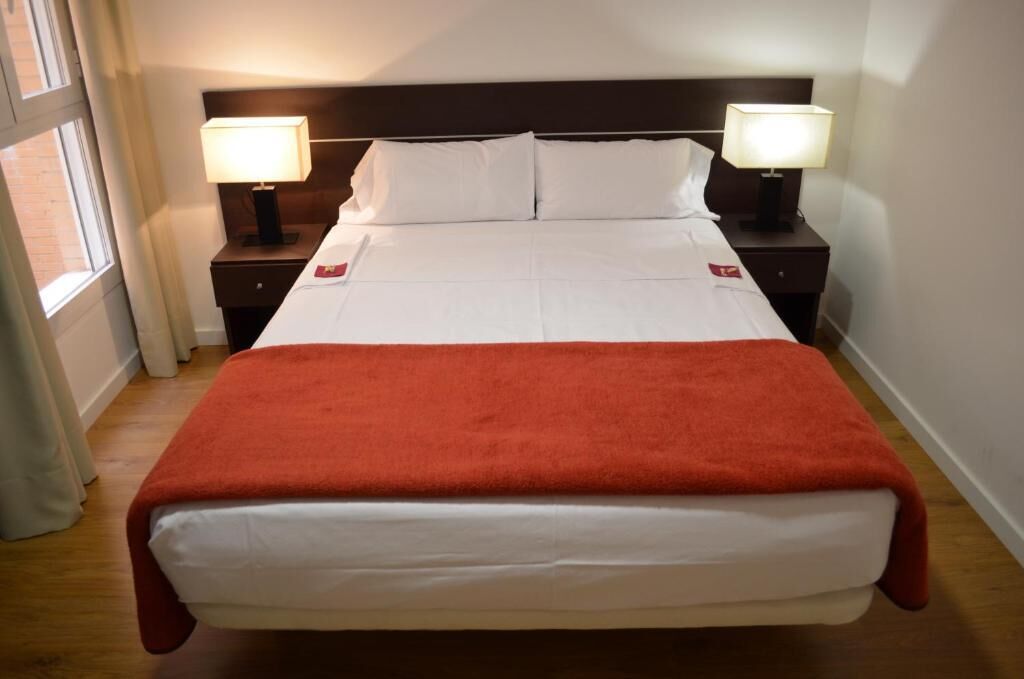 Een hotelkamer met een groot bed, twee nachtkastjes met lampen en een raam met gordijnen.