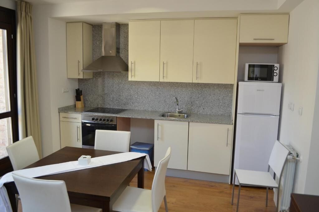 A compact kitchen with a stove, microwave, and refrigerator, a dining table with chairs, and a window with curtains.