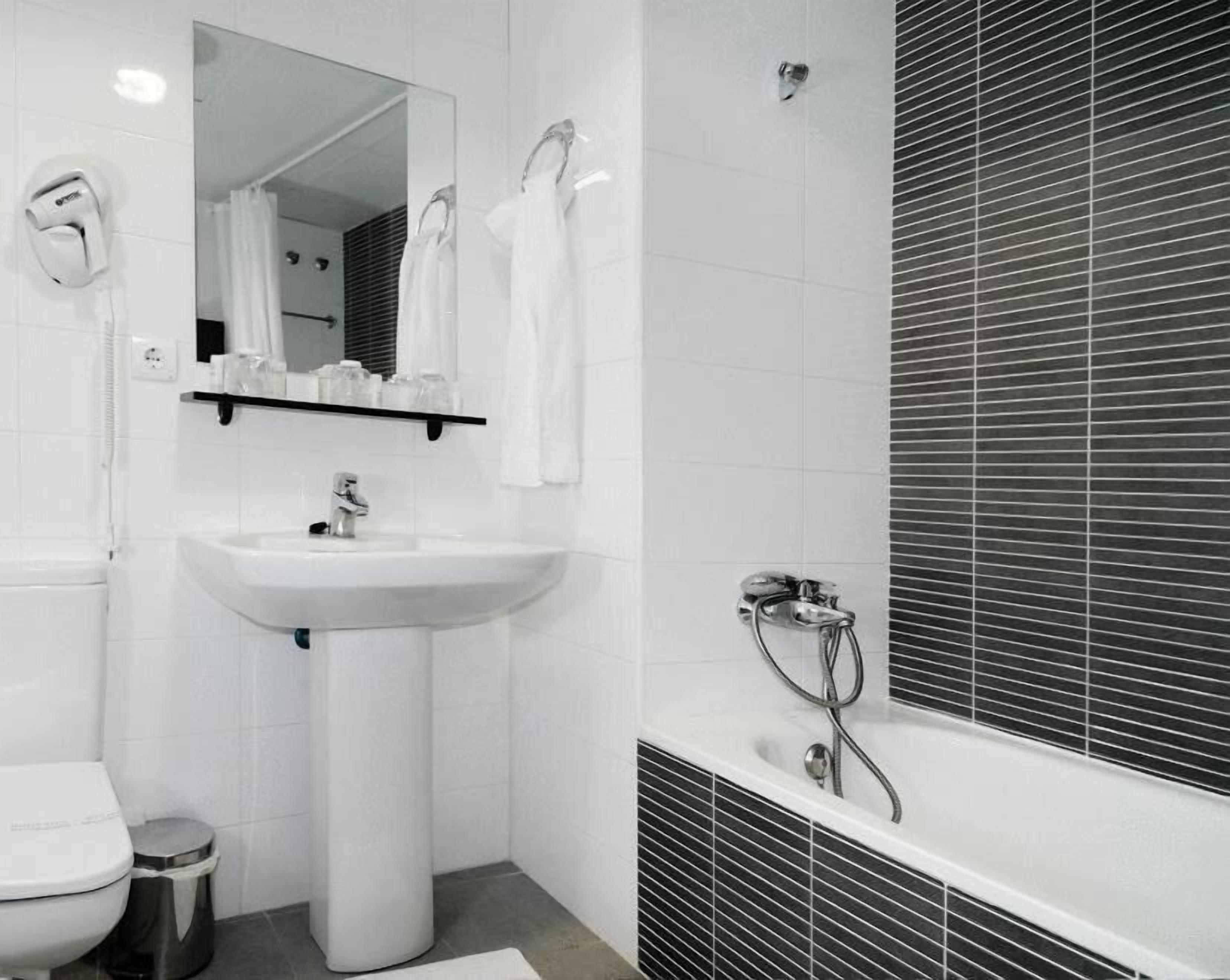 A bathroom with a white sink, a mirror, a toilet, and a shower area.