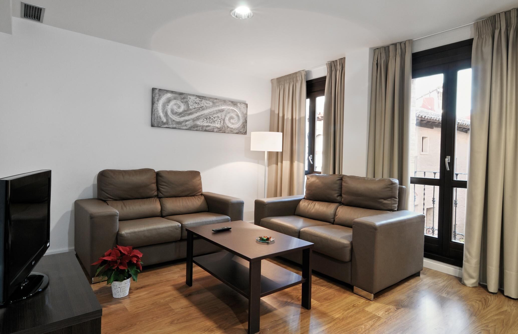 A modern living room with a sofa set, a coffee table, a TV, and a painting on the wall. - Apartamentos Los Sitios (Zaragoza)