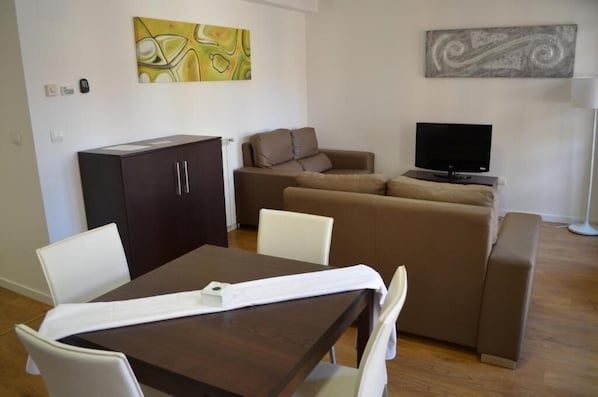 A living room with a sofa, a TV, a dining table with chairs, and artwork on the walls. - Apartamentos Los Sitios (Zaragoza)