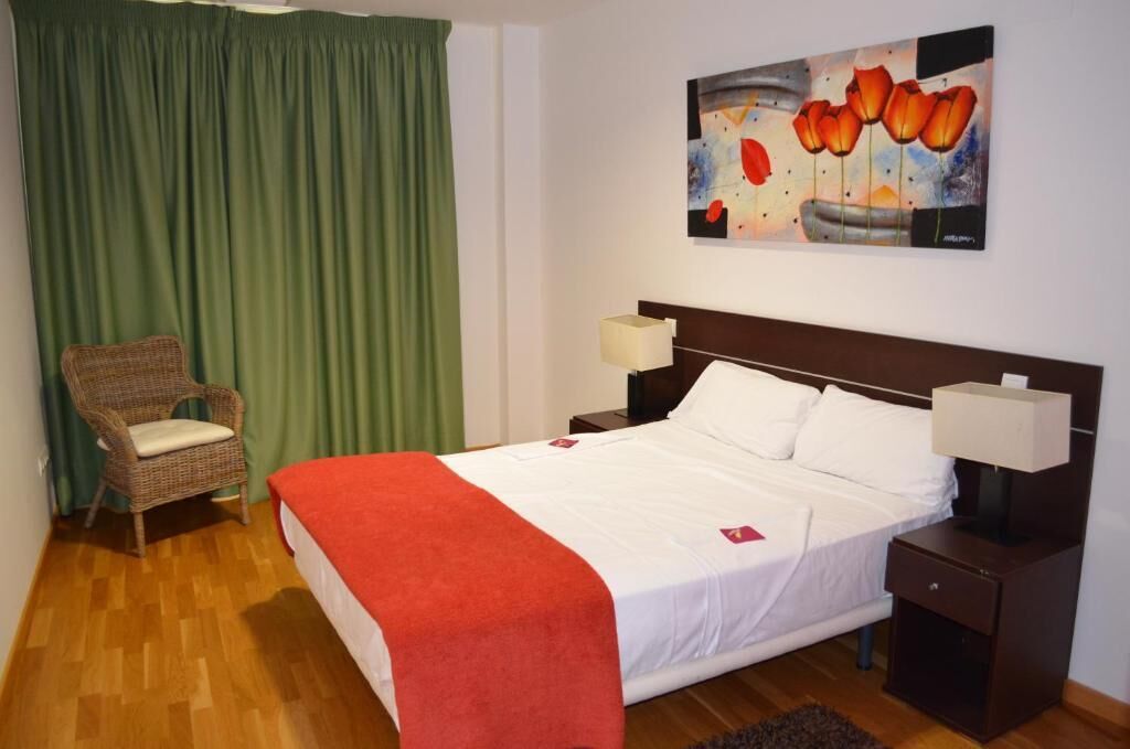 Une chambre d’hôtel avec un lit, une chaise, une table de chevet, une lampe et un tableau au mur.