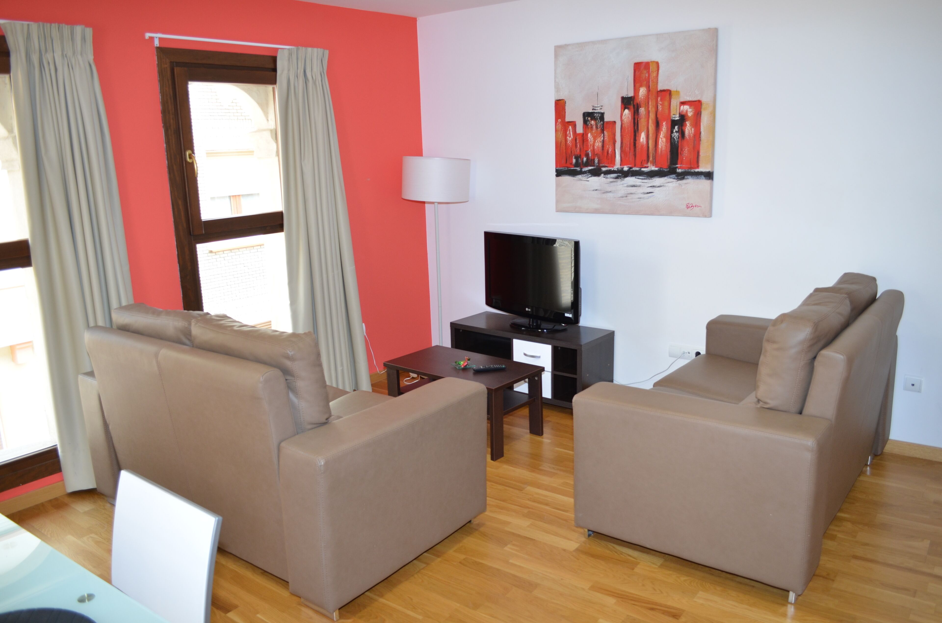 Ein Wohnzimmer mit zwei Sofas, einem Fernseher, einer Lampe und einem Bild an der Wand.
