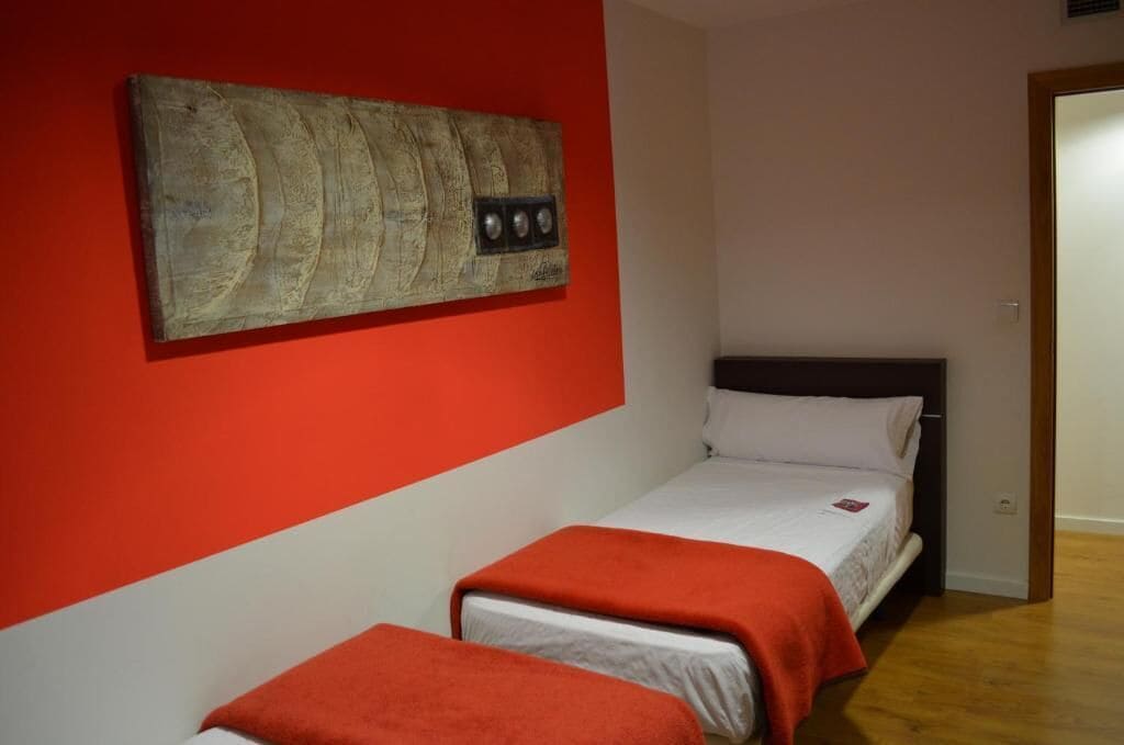 Una habitación con dos camas, una pared roja y suelo de madera.
