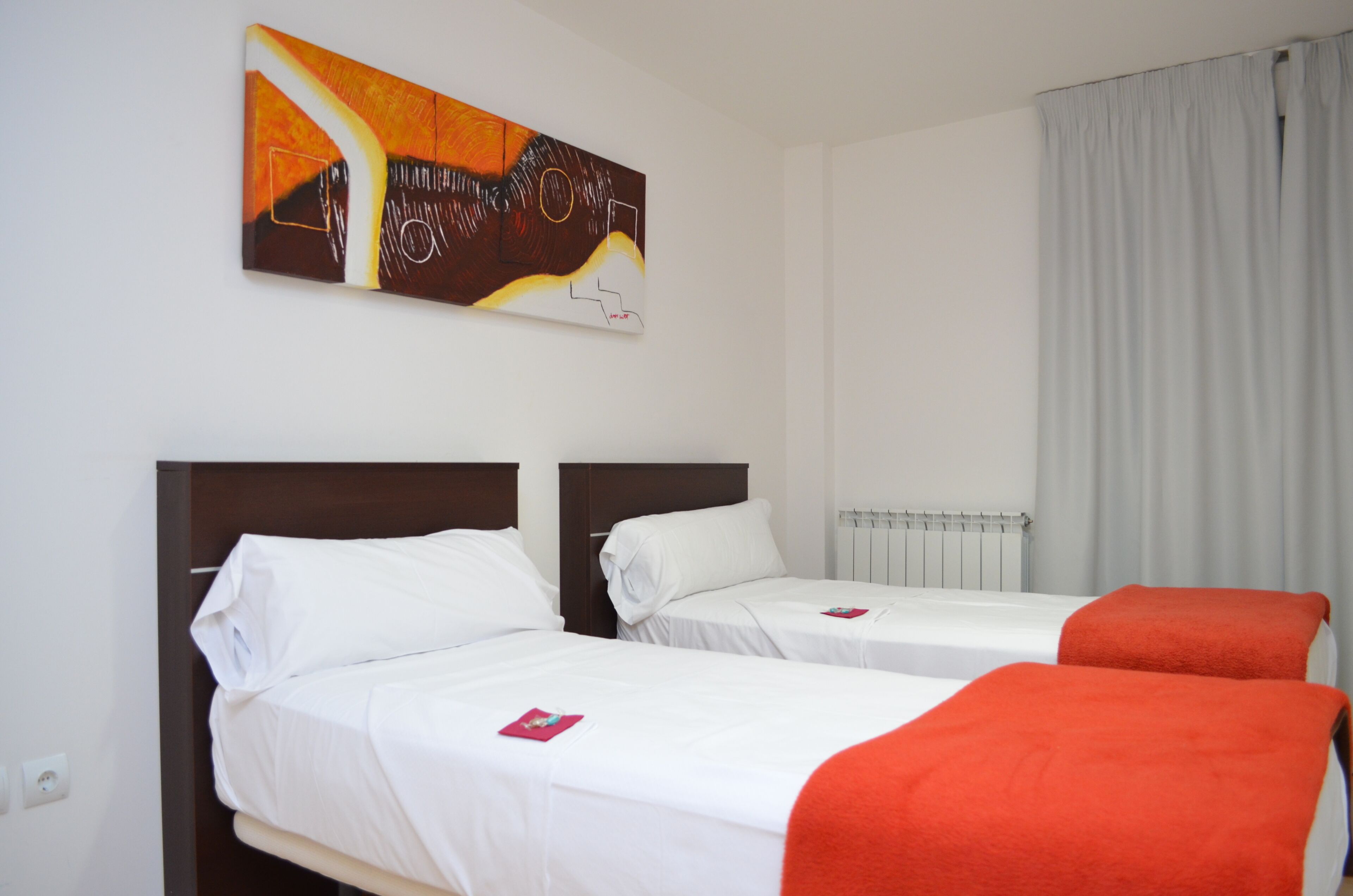 Habitación de hotel con dos camas, un cuadro en la pared, un radiador y una ventana con cortinas.