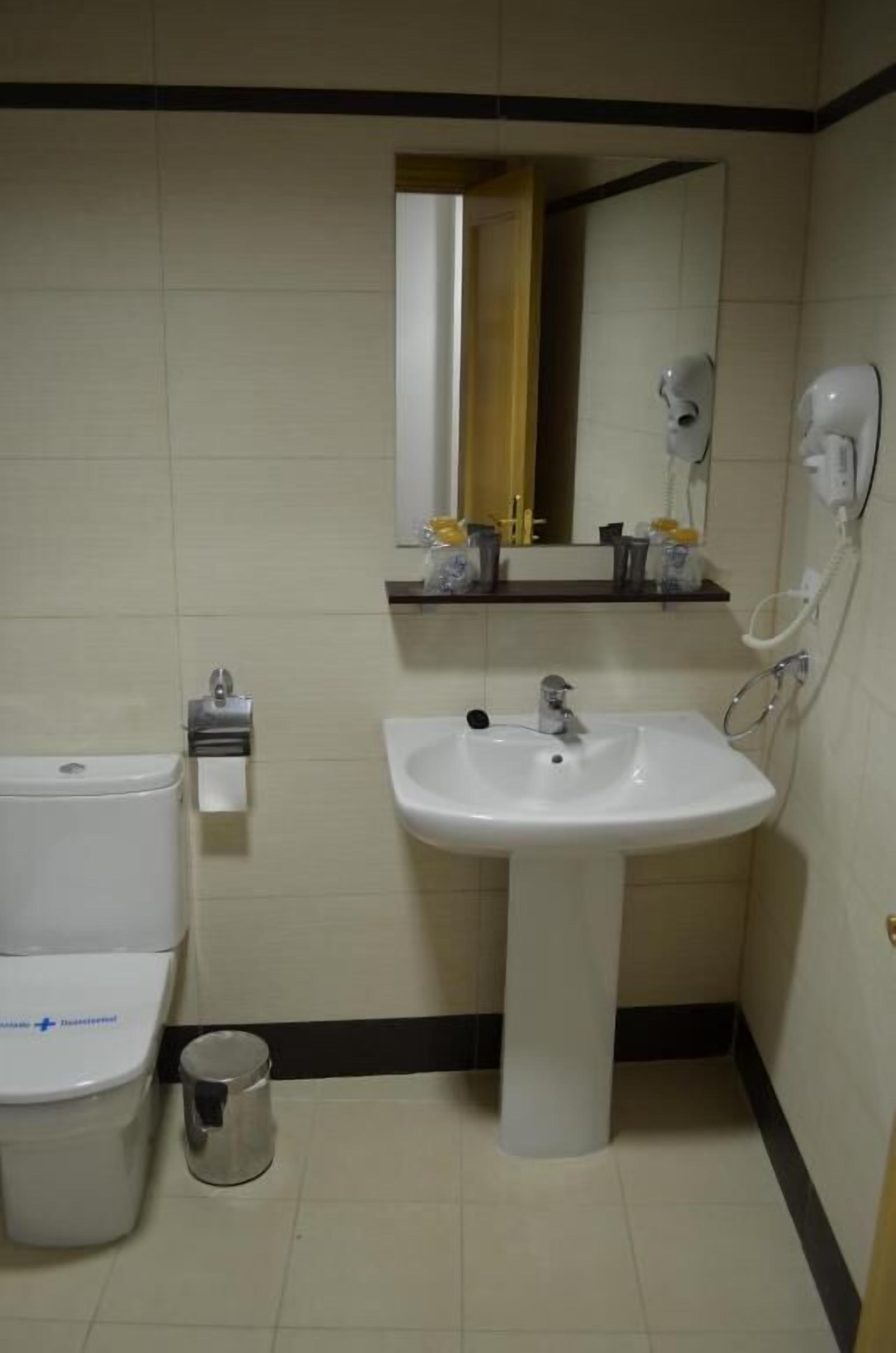 A bathroom with a toilet, sink, mirror, and hand dryer.