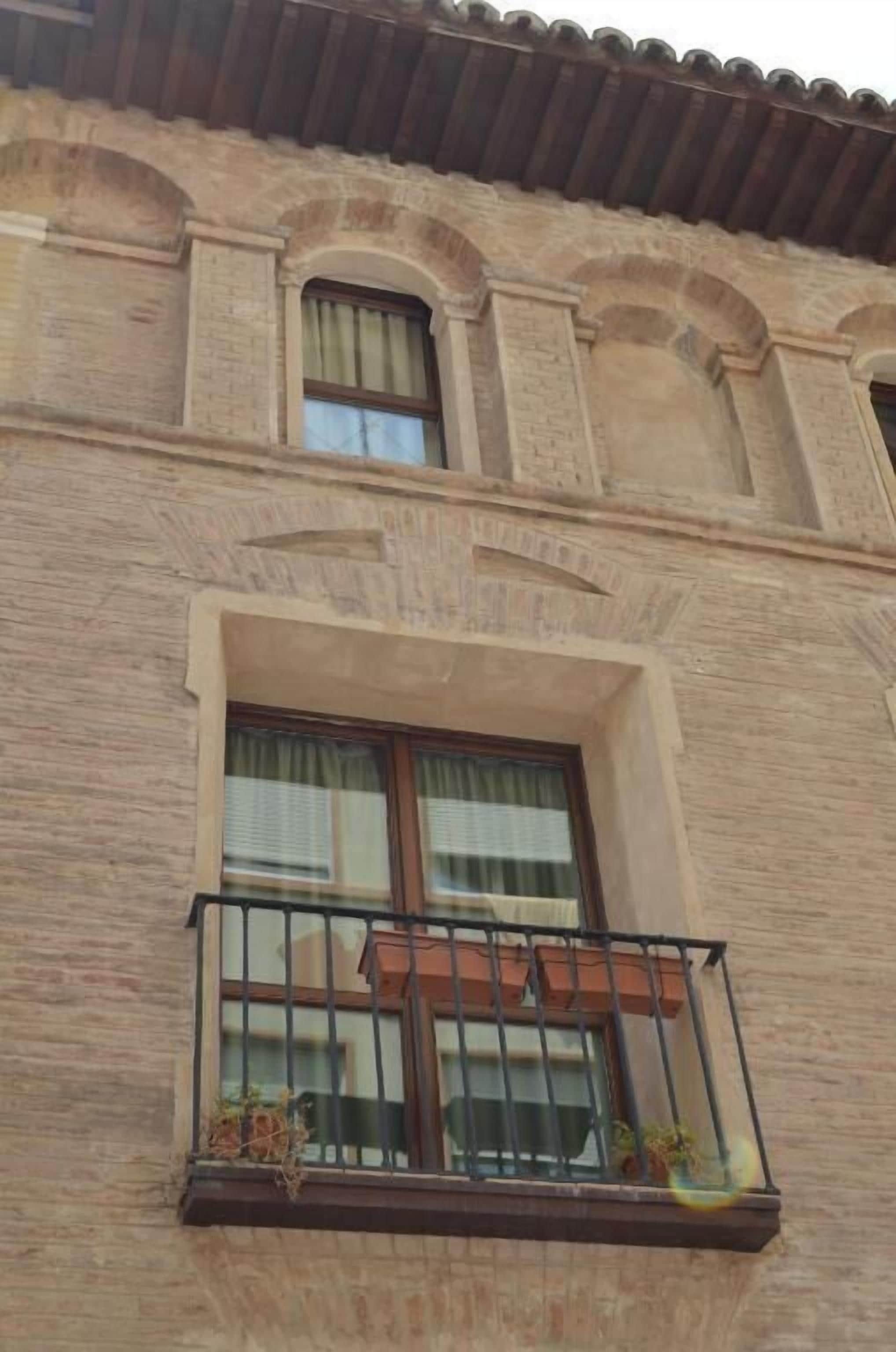 A building with a balcony, a window with a curtain, and a tiled roof.