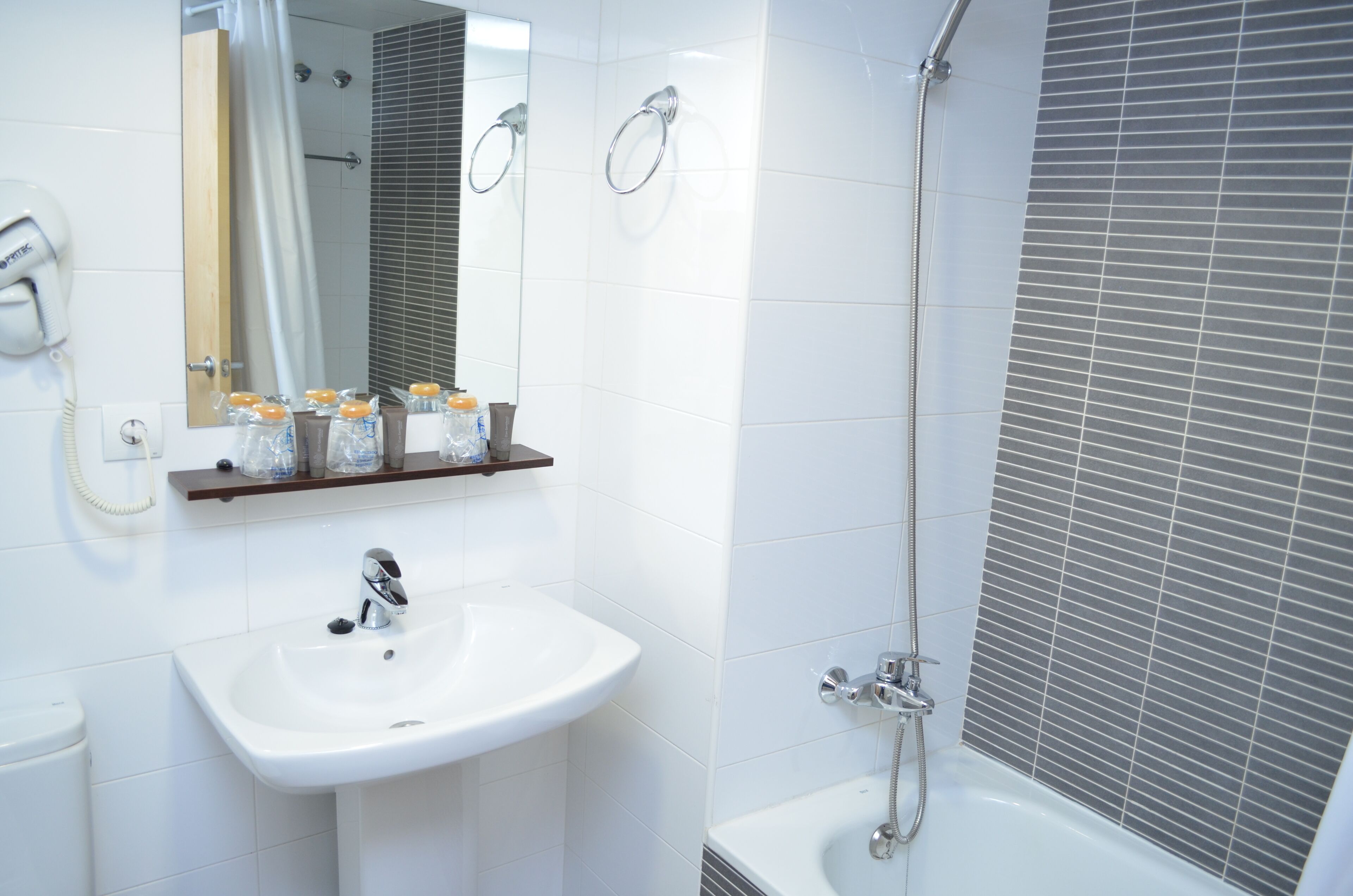 Ein Badezimmer mit weißem Waschbecken, einem Spiegel, einer Dusche und einer Toilette.
