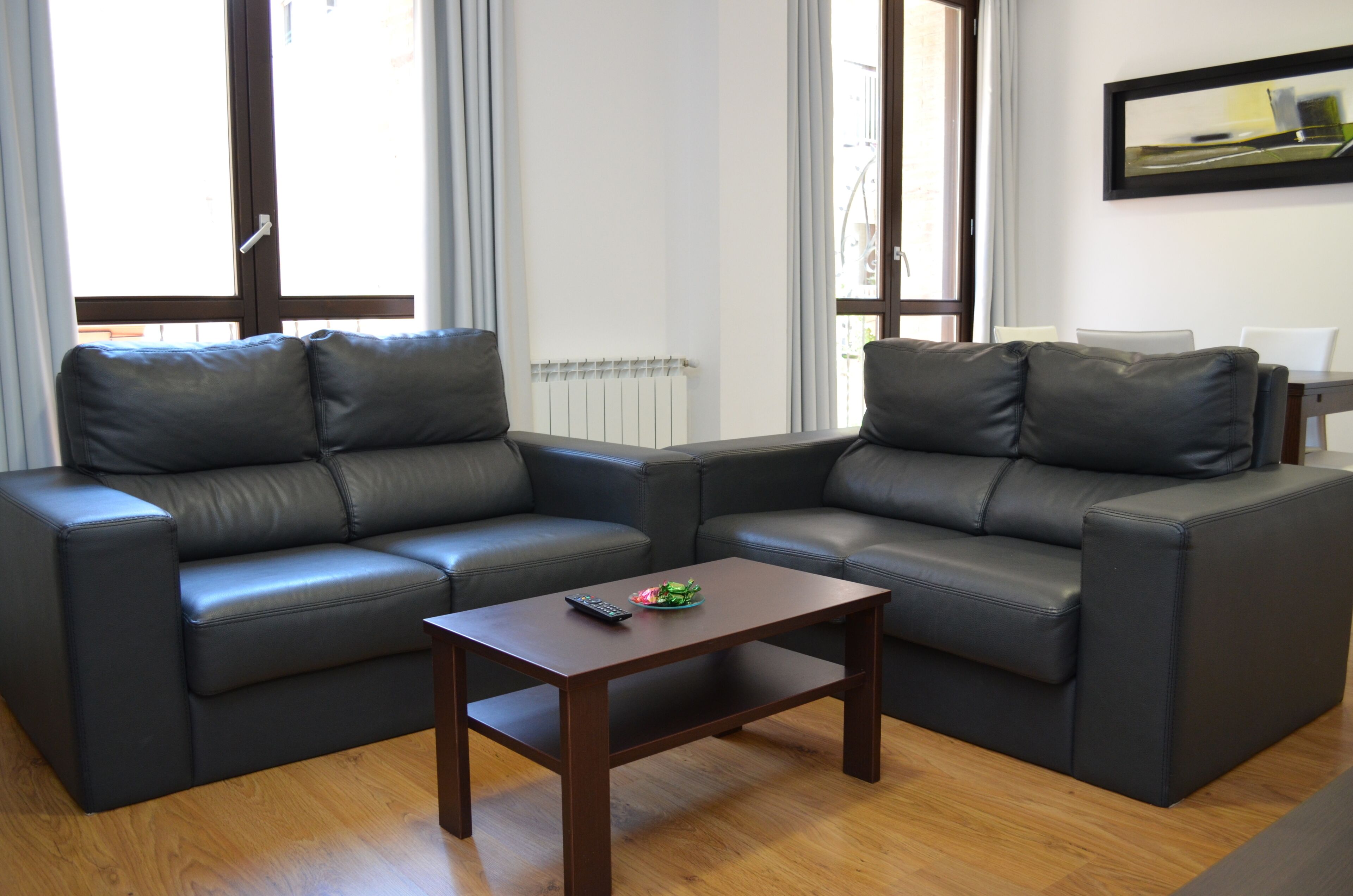Una sala de estar con dos sofás de cuero negro, una mesa de centro de madera y un radiador blanco.