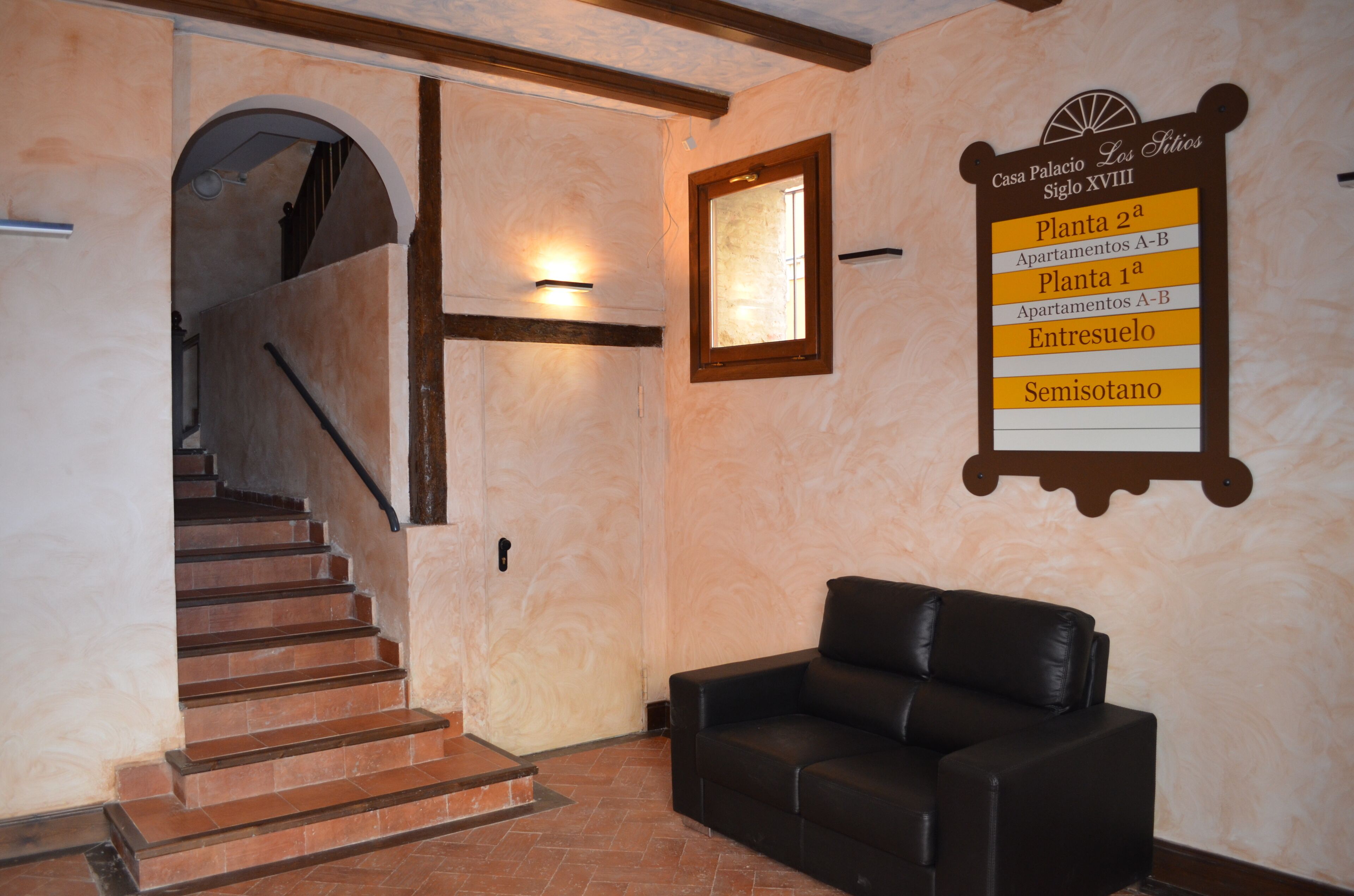 A hotel interior with a staircase, a black leather sofa, and a wall sign indicating room types.