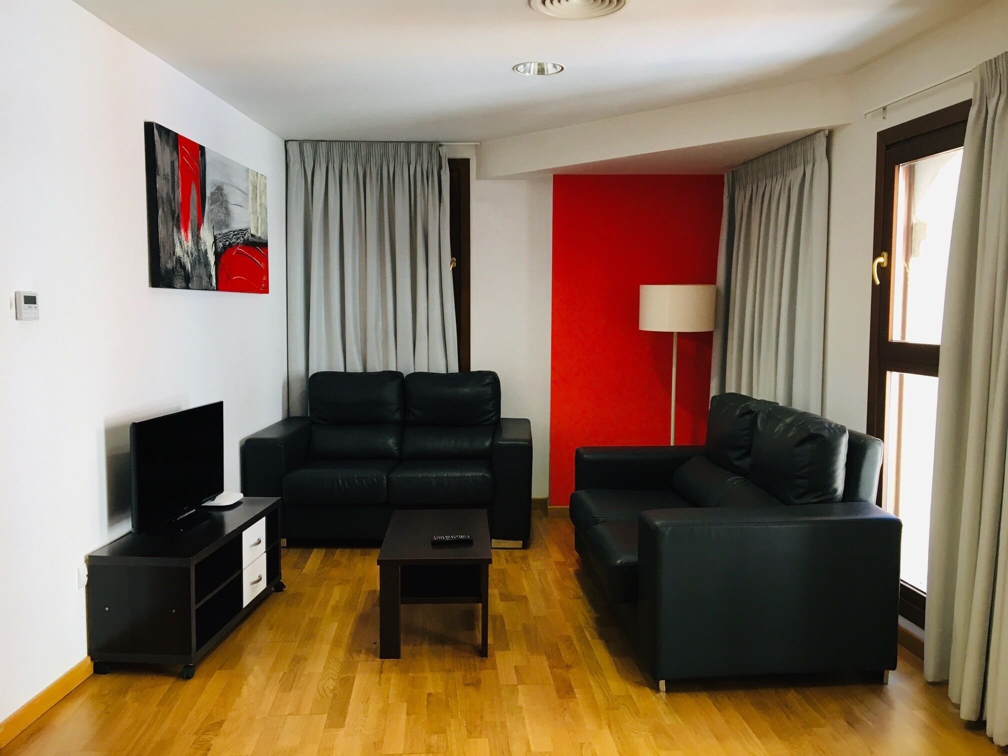 Una sala de estar con un sofá negro, un televisor, una mesita y una pared de acento roja.