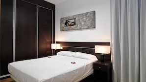 A hotel room with a bed, bedside lamps, a nightstand, a wall-mounted artwork, and a large window with curtains. - Apartamentos Los Sitios (Zaragoza)