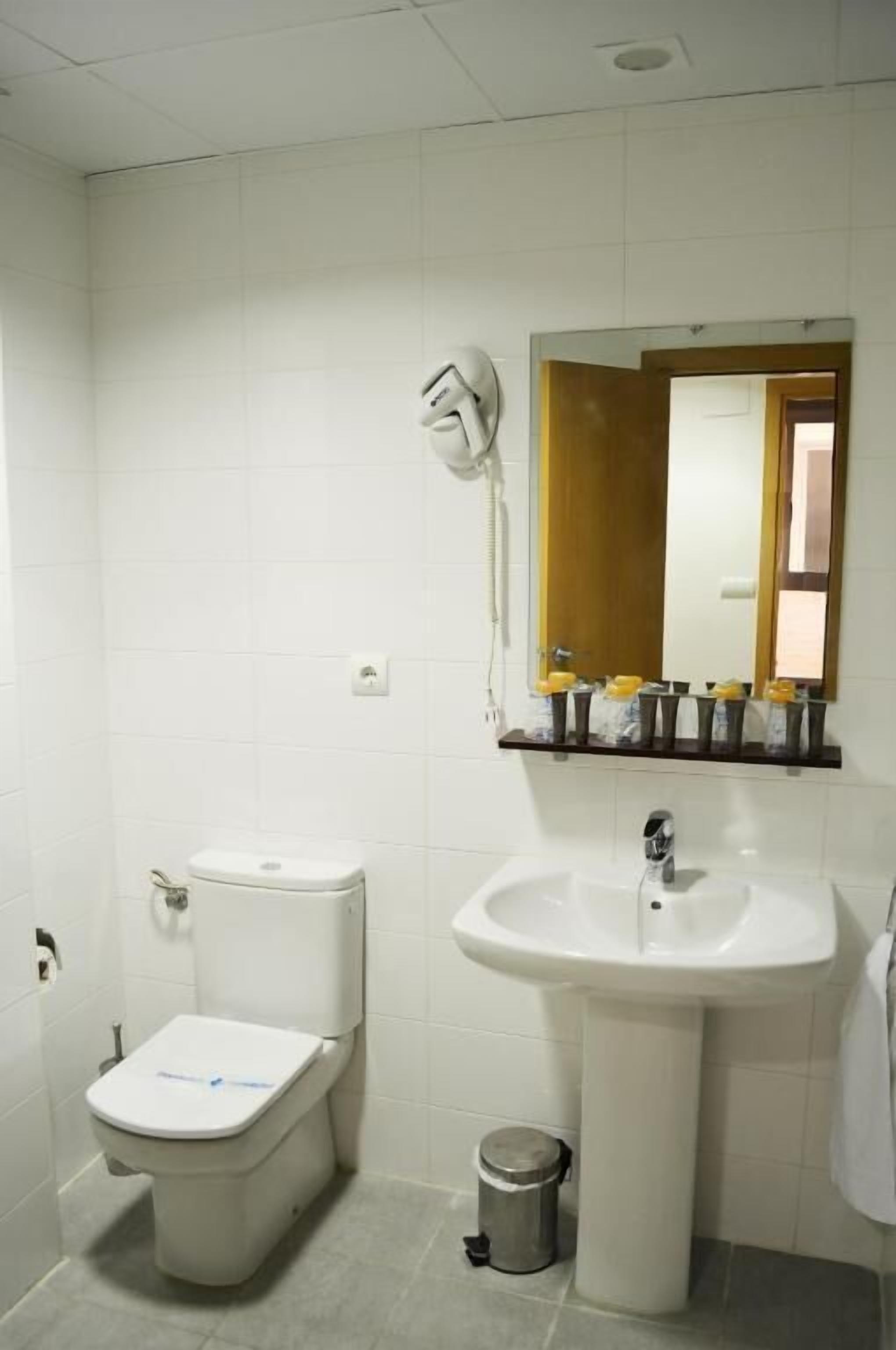Ein Badezimmer mit Toilette, Waschbecken, Spiegel und einem kleinen Mülleimer.