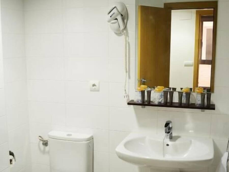 Ein Badezimmer mit Toilette, Waschbecken, Spiegel und einem kleinen Mülleimer.