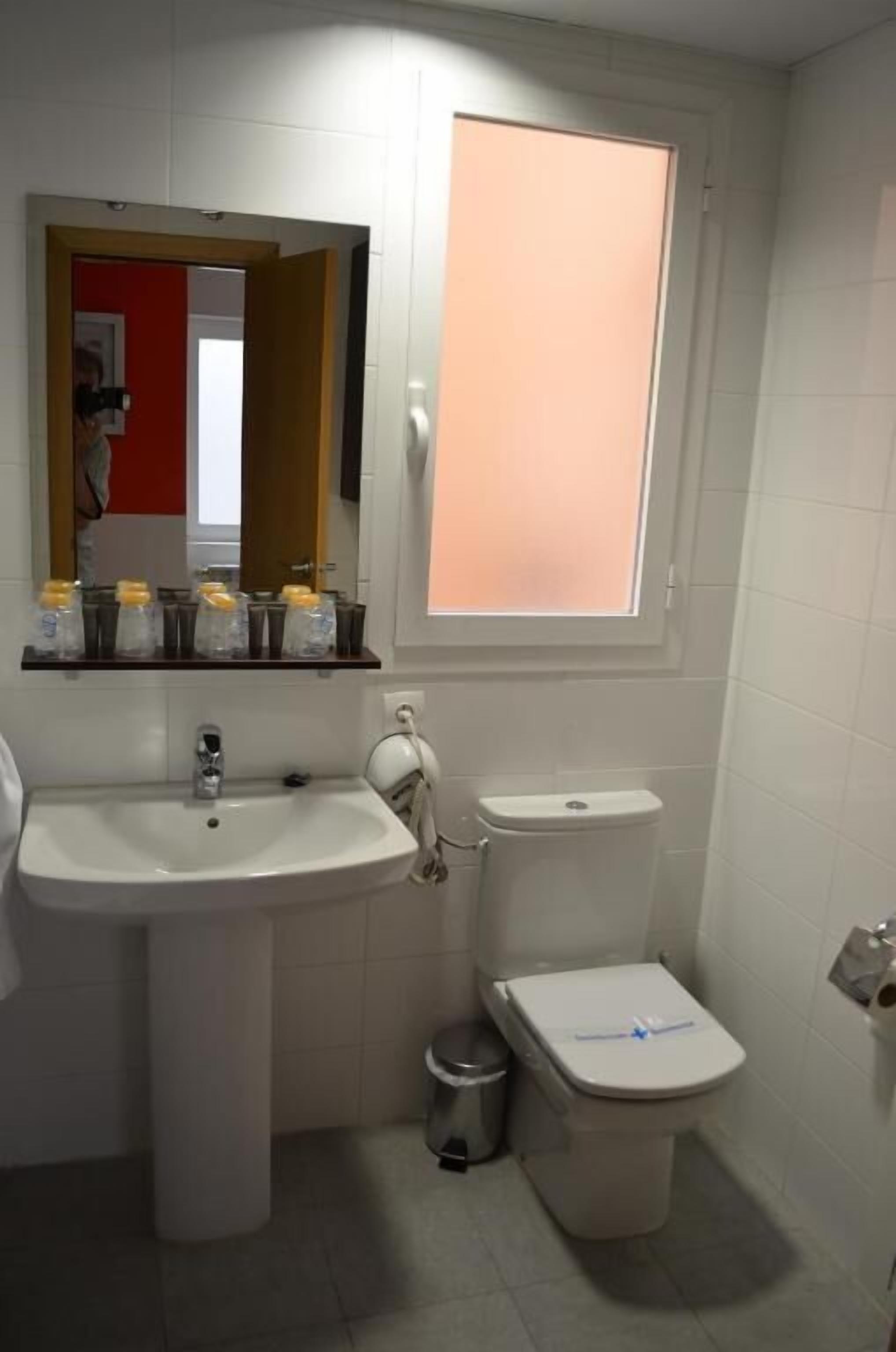 A bathroom with a white sink, a toilet, a window, and a mirror.