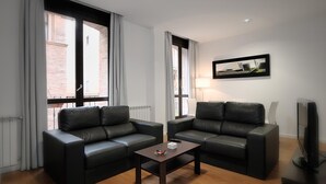 A modern living room with two black leather sofas, a small wooden coffee table, a flat-screen TV, and a framed picture on the wall. - Apartamentos Los Sitios (Zaragoza)