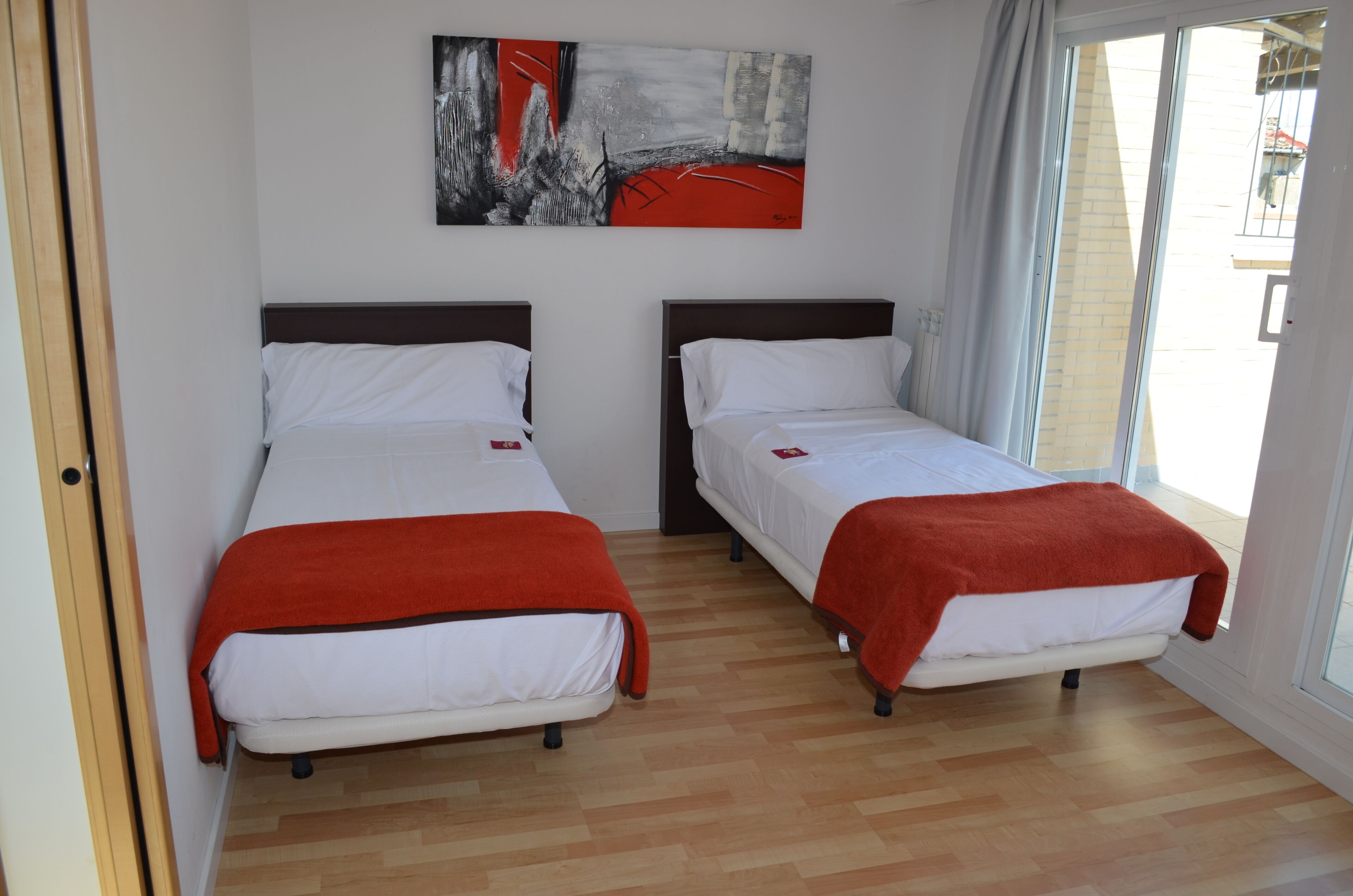 A room with two beds, a large window, and a painting on the wall.
