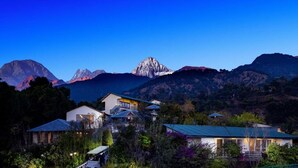 A mountain landscape with a prominent peak in the background, surrounded by residential buildings with visible windows and doors. - Rakkh Resort (Palampur)