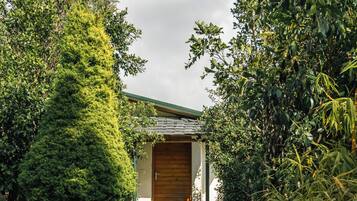 A pathway leading to a building with a wooden door, surrounded by lush greenery.