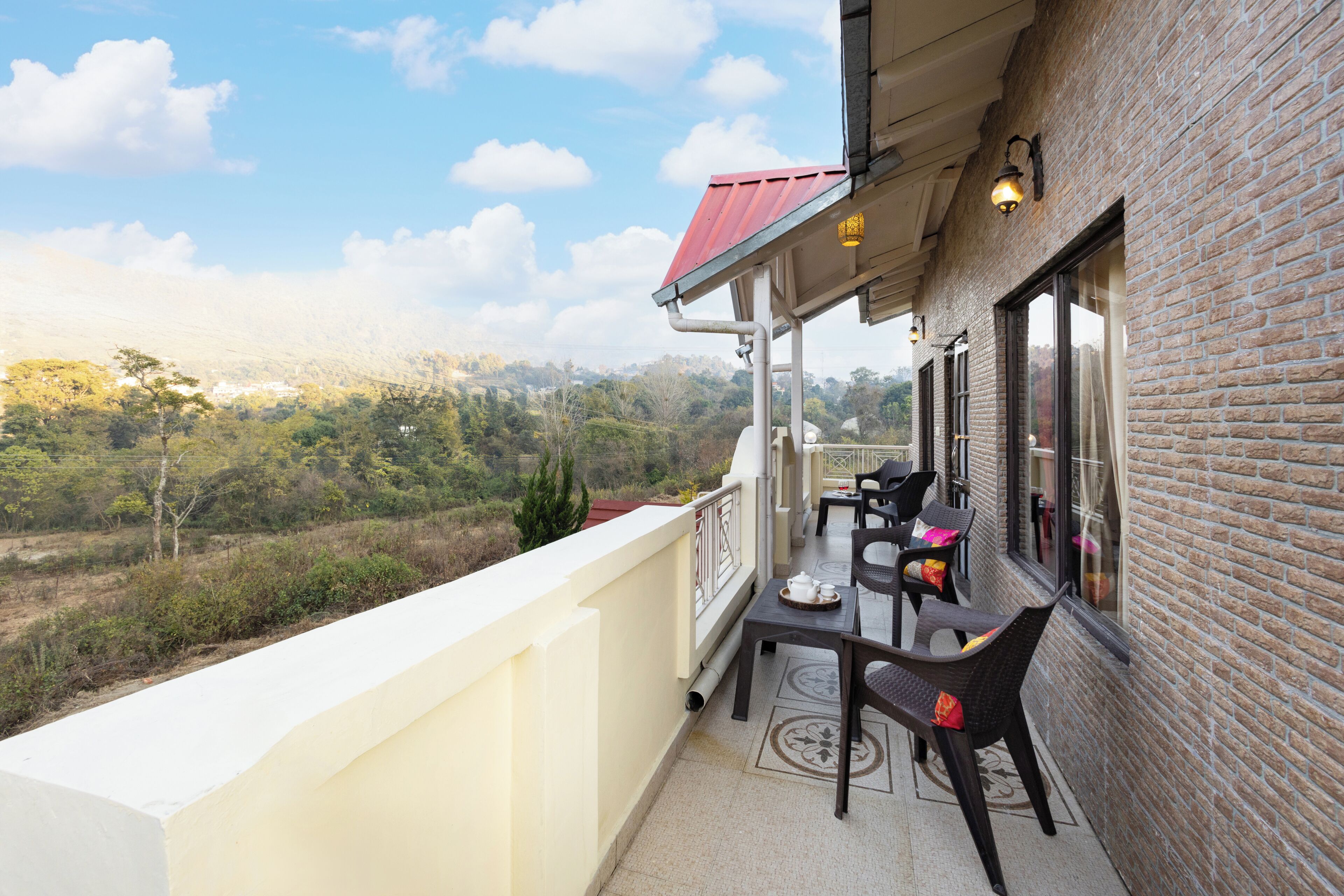 Ein Balkon mit Tisch und Stühlen, ein rotes Dach und Blick auf eine hügelige Landschaft.