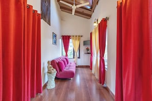 Un couloir avec des rideaux rouges, un plancher en bois, un canapé rose, un ventilateur de plafond et un téléviseur fixé au mur.