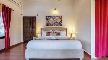 A bedroom with a large bed, a wooden door, a wall-mounted light fixture, and a window with red curtains.
